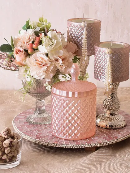 The Pearl Radiance Hamper is pure elegance. It includes two decorative candle holders, a glass jar with rose cashews, and a beautiful flower arrangement, perfect for sophisticated gifting.