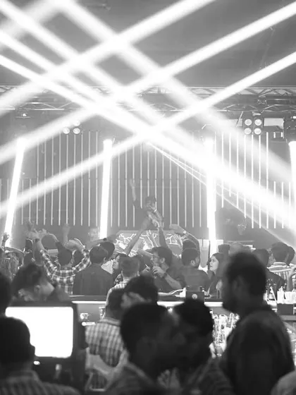 A dramatic black and white photo of the bar and dance floor, illuminated by powerful beams of light.