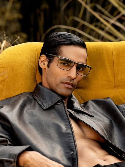 A relaxed portrait for John Jacobs, with the model seated in a yellow armchair amidst tall grass, creating a cool, edgy vibe.