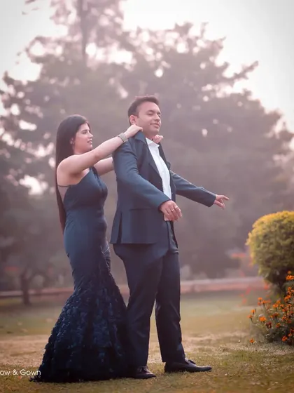 A playful and candid moment during a pre-wedding shoot in a park. The woman adjusts her partner's suit jacket, creating a natural and interactive photo that shows their connection.