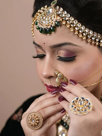 A close-up on the details of a student's bridal makeup, focusing on the eye makeup and the traditional nath.
