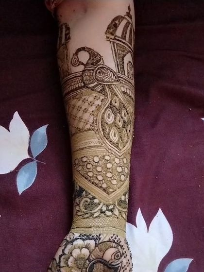 A full view of a bridal arm design featuring a peacock and architectural elements like domes. This narrative style of henna is perfect for telling a bride's personal story.