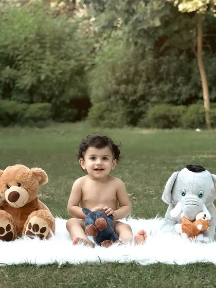A baby boy sits happily on a white fur rug in a park, lined up with his favorite stuffed animals. This creative shot is a sweet representation of his first year of friendships.