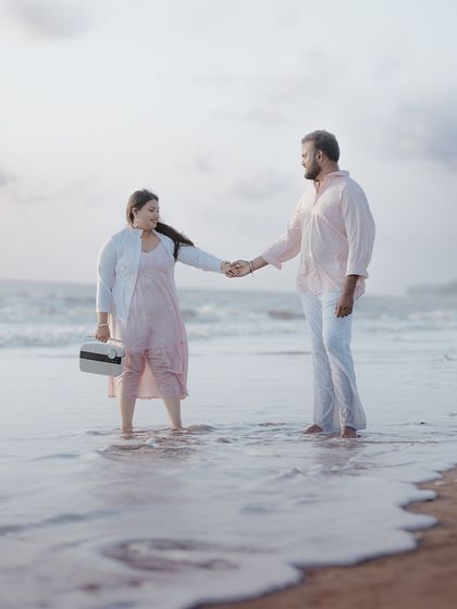 A couple holding hands in the shallow waters of the beach, with a vintage-style radio adding a unique prop to their pre-wedding story.