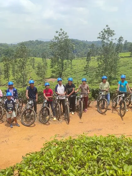 A group of young mountain bikers poses with their cycles against the backdrop of Coorg's rolling tea gardens.
