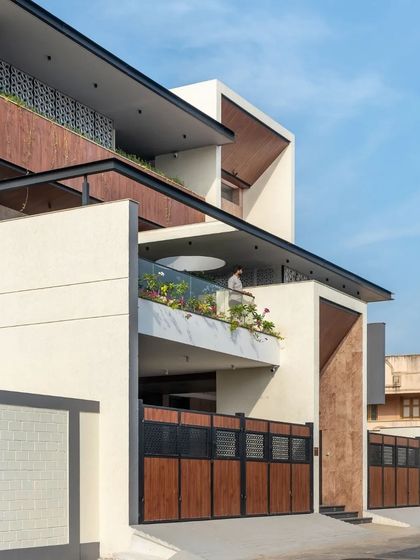 The combination of white stucco, wood paneling, and patterned jali screens creates a visually rich and layered exterior.