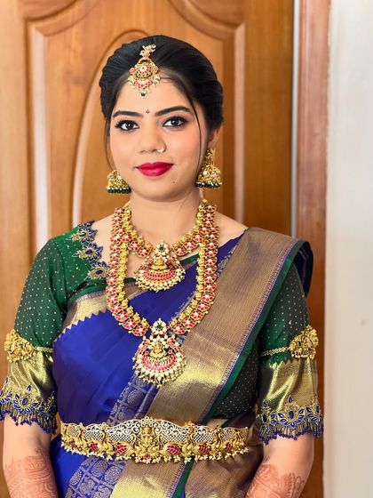 A classic bridal portrait. The makeup is traditional with a modern touch, using a bright red lip to complement the blue and green saree.