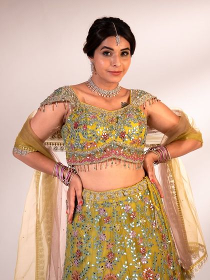 A close-up of the intricately embroidered blouse on this lime green lehenga. The mirror work and colorful threads are perfect for a festive celebration.