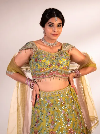 A close-up of the intricately embroidered blouse on this lime green lehenga. The mirror work and colorful threads are perfect for a festive celebration.