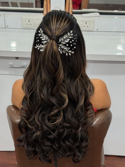 A modern half-up, half-down hairstyle with soft waves and highlights, elegantly finished with a sparkling bow-shaped hair clip. Perfect for a reception or sangeet.