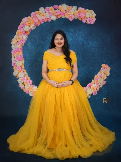 Let us bring your dreams to life with our creative prop setups. Here, our client shines in a vibrant yellow gown, seated on a floral crescent moon prop that adds a touch of magic and whimsy to her maternity portrait.