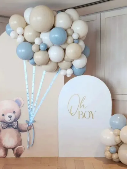 An adorable "Oh Boy" teddy bear themed baby shower. The setup features a cute teddy bear cutout holding a bunch of balloons made from real balloons, against a clean, arched backdrop.