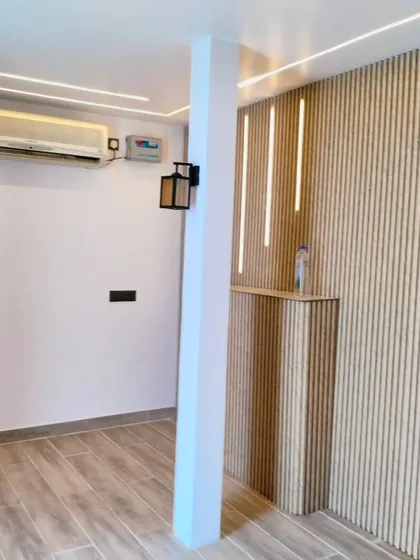 The interior of a newly constructed terrace room, featuring wood-look flooring and a stylish slatted wall with integrated vertical LED lights.