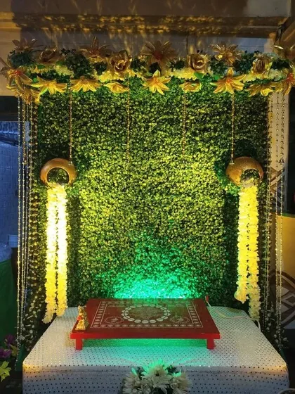 This Navratri mandap decoration uses a green wall as a backdrop, accented with hanging marigold flowers and traditional earthen pots for an eco-friendly and traditional look.