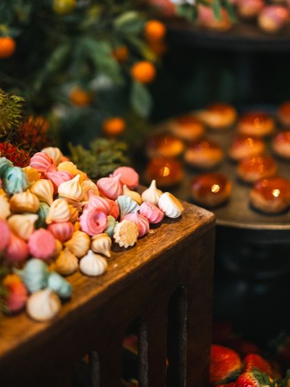 Colorful meringue kisses add a touch of whimsy and color to the dessert section of our grazing table. They are nestled in a wooden crate next to fresh strawberries.