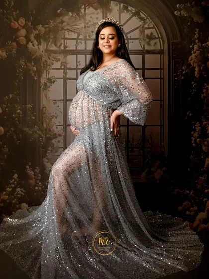 A full-length portrait in a stunning silver sequin gown. The floral archway backdrop adds a touch of romance and elegance to this glamorous maternity photo.