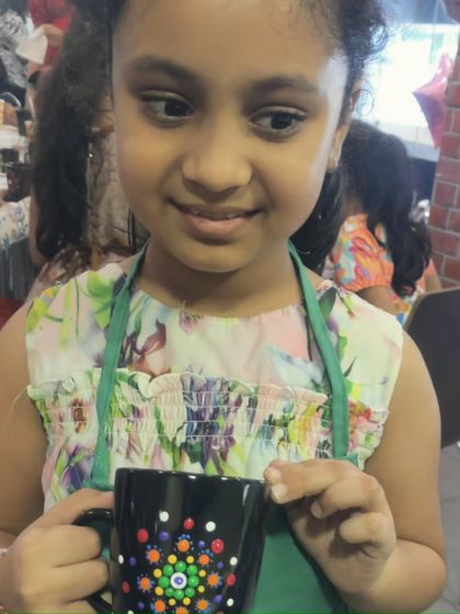 A close-up of a young girl admiring the dot mandala design she just finished painting on her mug.