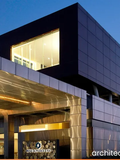 The entrance of the India Glycols headquarters features a striking contrast between the dark upper volume and the metallic lower structure. This design creates a powerful sense of arrival while hinting at the building's modern, industrial function.