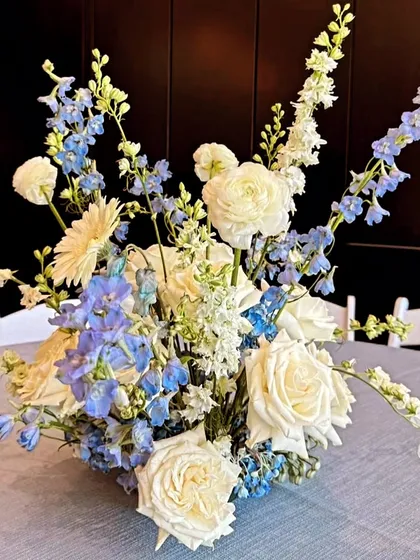 A fresh and beautiful floral centerpiece for a table, using a mix of white roses and blue delphiniums for a classic and elegant look.