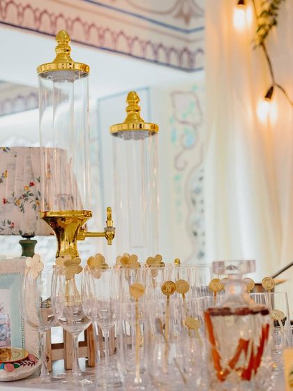 A vintage-style bar setup with ornate glass beverage dispensers and gold-rimmed glasses.