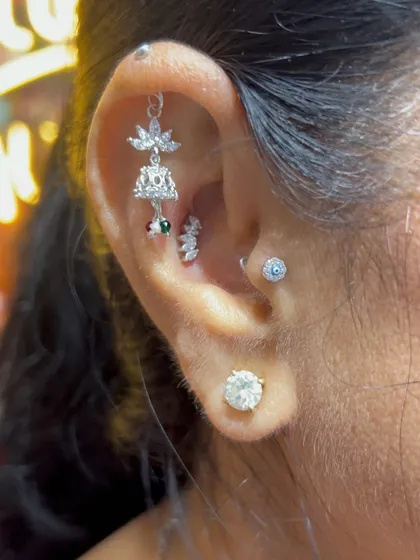A traditional jhumka-style hanging brings a touch of Indian heritage to this modern ear stack, complemented by an evil eye stud and a solitaire.