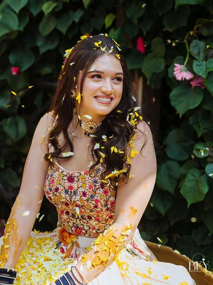 A candid portrait of the bride smiling, her face and hair adorned with turmeric and flower petals.