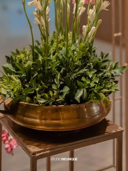 A brass bowl filled with fresh greenery and tuberoses, placed next to a decorative screen. These small touches add life and elegance to every corner of the venue.