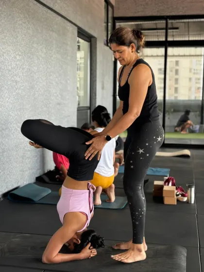 Guiding a student into a stable headstand requires careful attention to their alignment. Here, I'm ensuring her foundation is strong and her spine is protected as she lifts into the pose.