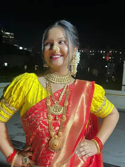 A full view of a client against a city skyline at night. This shows how the traditional red saree, gold jewellery, and expert draping create a stunning silhouette.