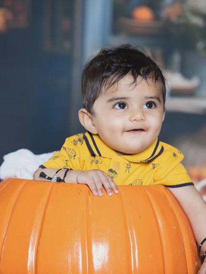 A happy baby boy peeking out of a giant pumpkin.