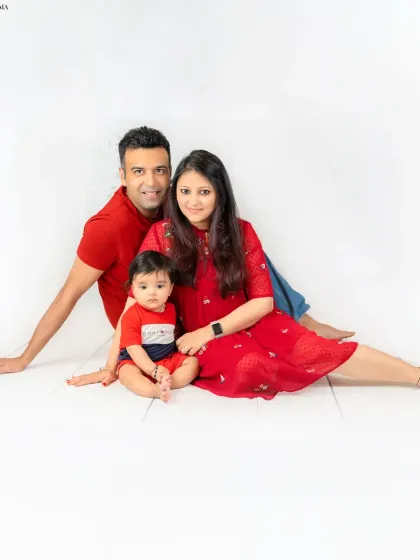 A full family portrait against a clean white backdrop. The coordinated red outfits make the family pop in this classic, seated photograph.