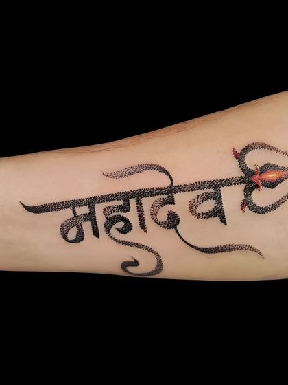 A dotwork style "Mahadev" script tattoo on the forearm. The stippling technique gives the lettering a unique texture and look.