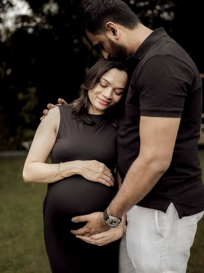 A tender and protective embrace. He kisses her forehead as they both gently hold the baby bump, a portrait of quiet love and anticipation.