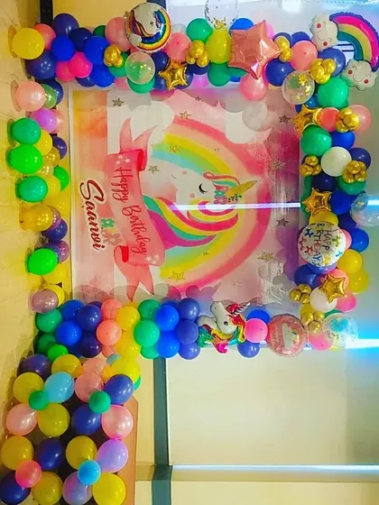 A square balloon frame in bright rainbow colors, creating a photo booth with a custom unicorn backdrop.