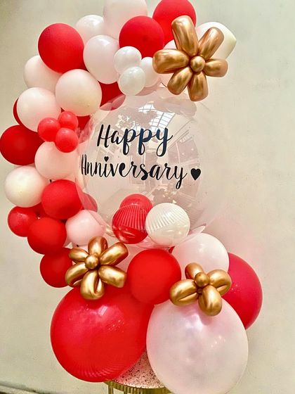 A beautiful and modern anniversary balloon bouquet. The clear bubble balloon with a custom "Happy Anniversary" message, surrounded by red and white balloons with gold floral accents, is a chic way to celebrate another year together.