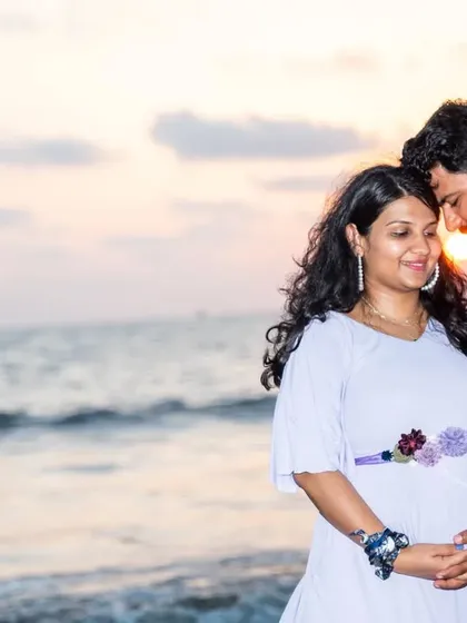 An intimate sunset portrait on the beach. The golden light creates a warm, romantic glow around the expecting couple.