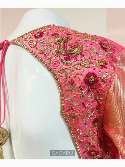 A statement back design for a Kanjeevaram saree blouse. This piece features intricate floral and peacock motifs embroidered in zardosi and thread work on a bright pink fabric.