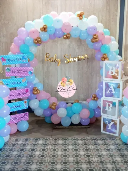 A complete gender reveal party setup with a circular balloon arch, 'BABY' blocks, and themed signposts.