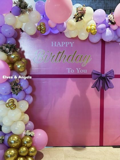 A beautiful birthday backdrop designed to look like a giant gift box, complete with a purple bow and a lovely balloon garland.