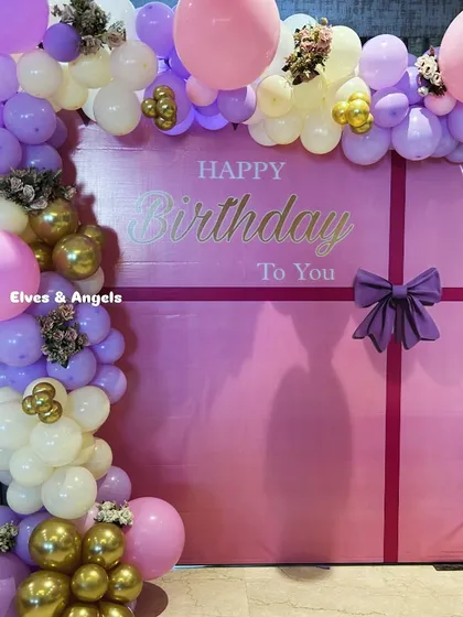 A beautiful birthday backdrop designed to look like a giant gift box, complete with a purple bow and a lovely balloon garland.