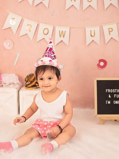 Ready for the party to start! This little one is all smiles with her birthday hat on, next to a sign that reads "Frosting & Fun, I'm One".