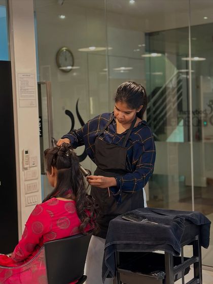 A student carefully styles a client's hair after a cut, learning how to complete the service with a professional finish.