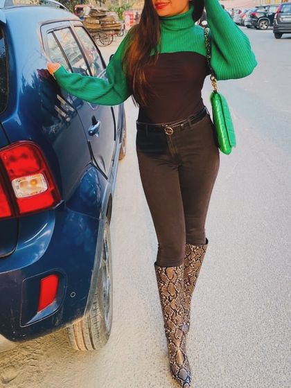 A stylish winter outfit featuring a green and brown turtleneck, dark jeans, and snakeskin boots.