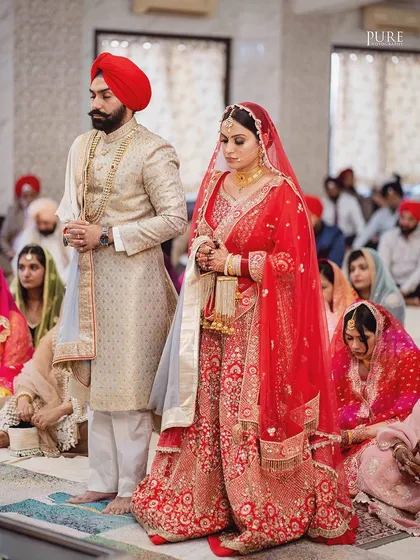 The bride and groom standing in prayer during their Anand Karaj. The focus is on their devotion and the solemnity of the Sikh wedding ceremony.