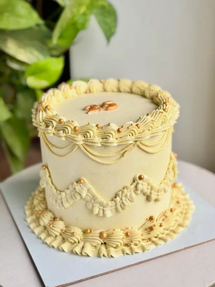 A slightly different angle of the golden vintage cake, showcasing the "25" topper and the beautiful texture of the buttercream piping against a leafy background.