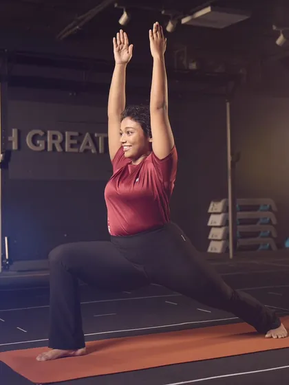 Holding Virabhadrasana I, or Warrior 1 pose, in a calm studio setting. This foundational yoga pose builds strength in the legs and core while opening the chest and shoulders. It's a perfect example of how I use yoga to create stability and power from the ground up.