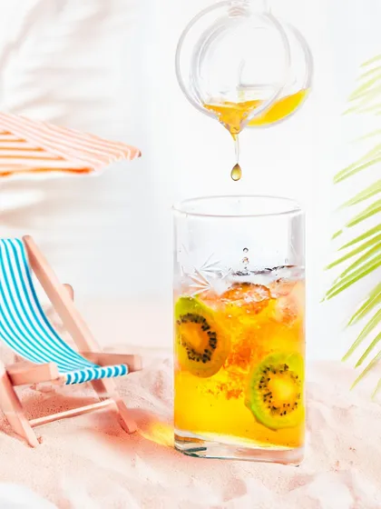 A bright, high-key shot of a summery iced tea, using a miniature beach scene to create a playful, vacation-themed product photo.