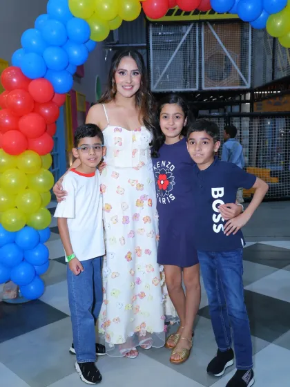 A guest poses with a group of children under a colorful balloon arch. Our parties are all about bringing people together for a happy celebration.