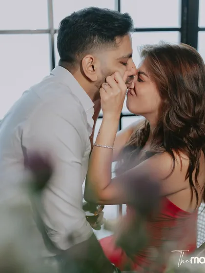 A close, intimate kiss between the couple, framed by soft-focus elements in the foreground. This romantic shot captures a private moment in their celebration.