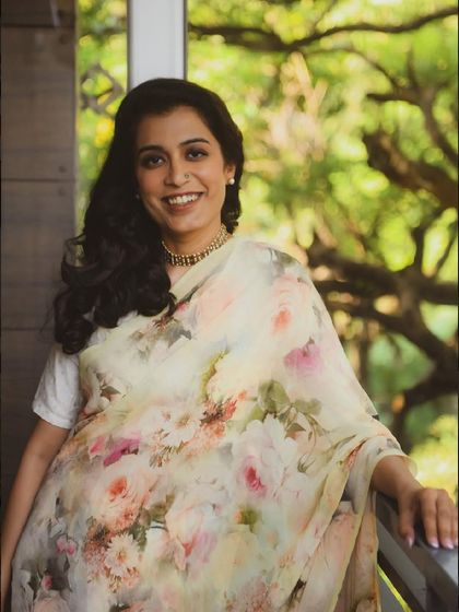 A bright, happy portrait of a woman in a floral sari, smiling against a lush green background. It’s a celebration of natural beauty.